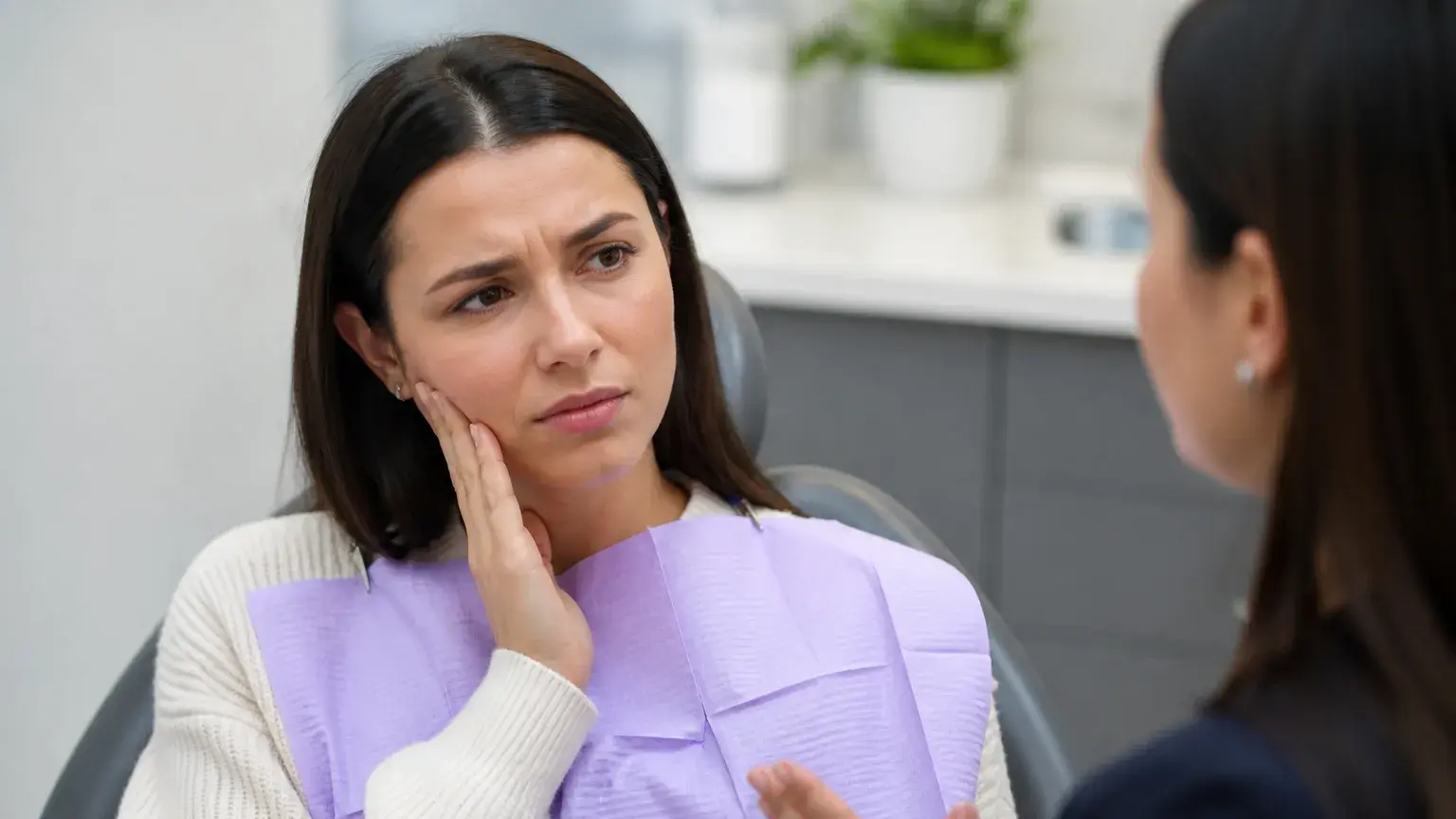 Patient holding jaw beside TMJ and TMD anatomy models during a dental bite pain explanation