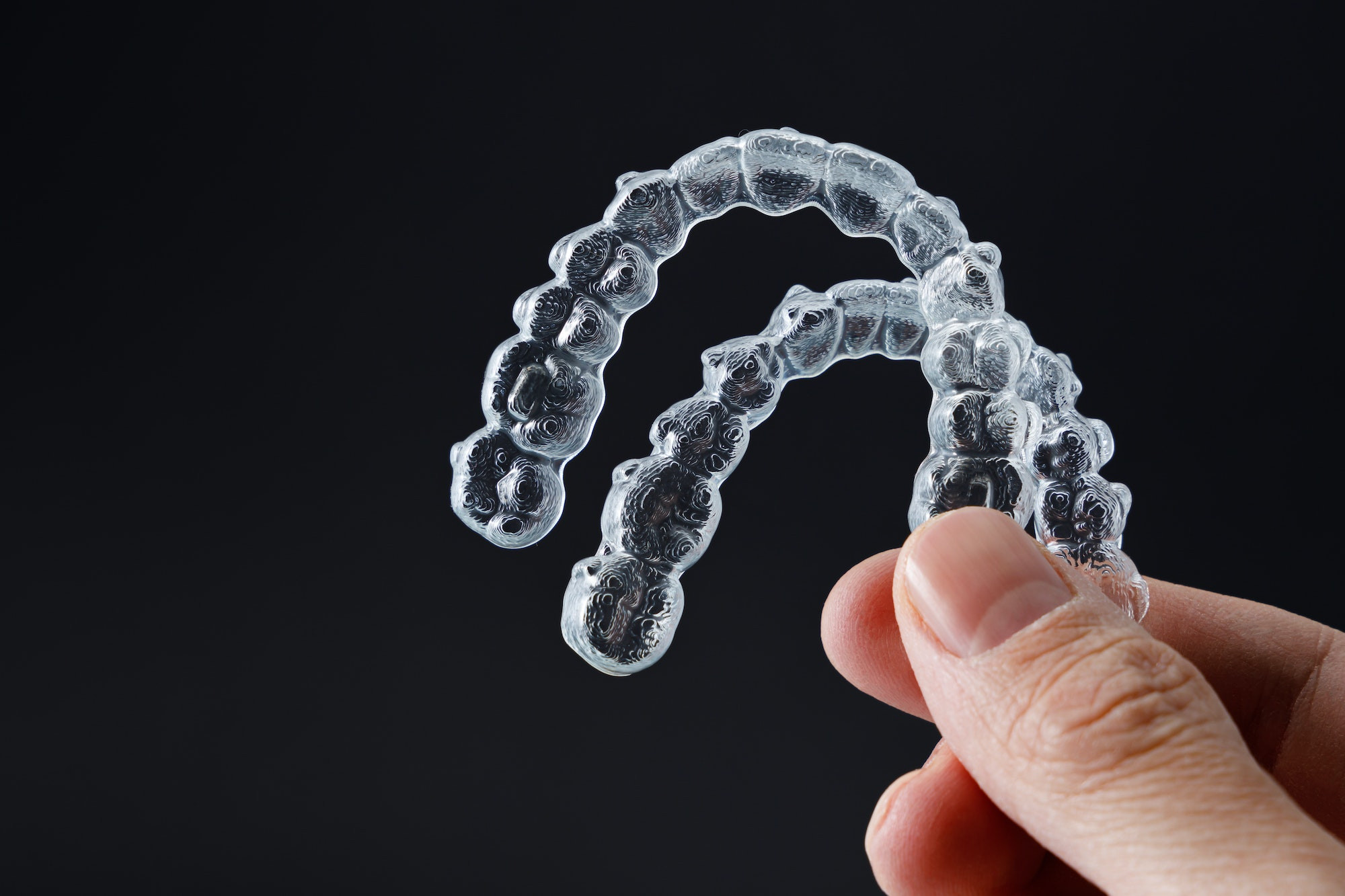 Clear aligner trays held in hand representing Invisalign and ClearCorrect doctor-directed orthodontic options