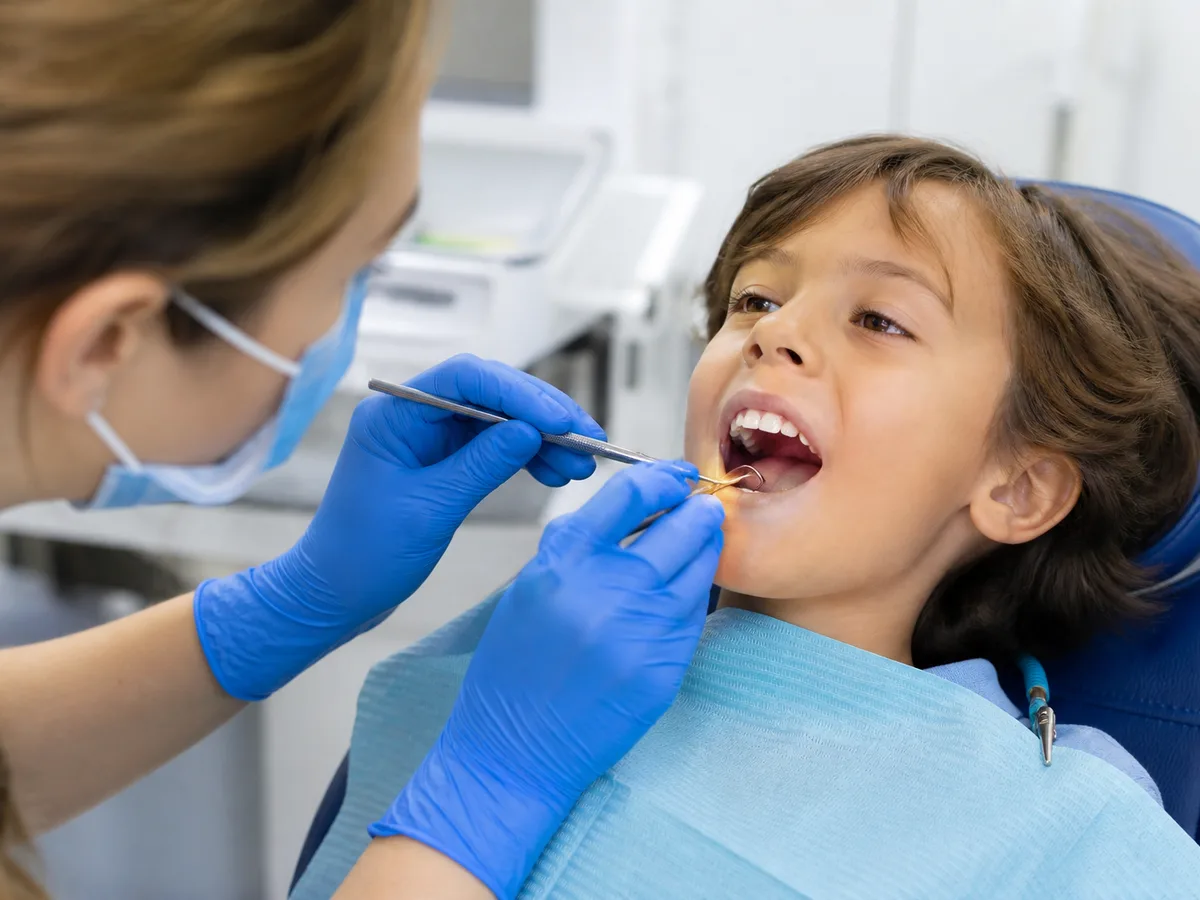 Child smiling with a missing front tooth while a parent schedules a dental check