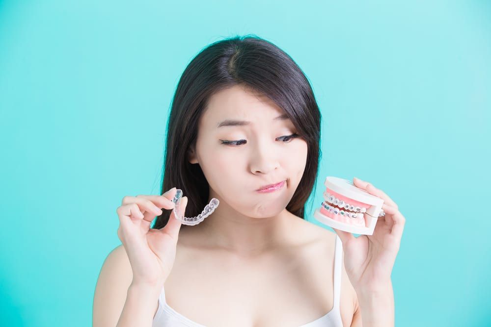 Blue background asian girl making choices between aligners or braces tough decision