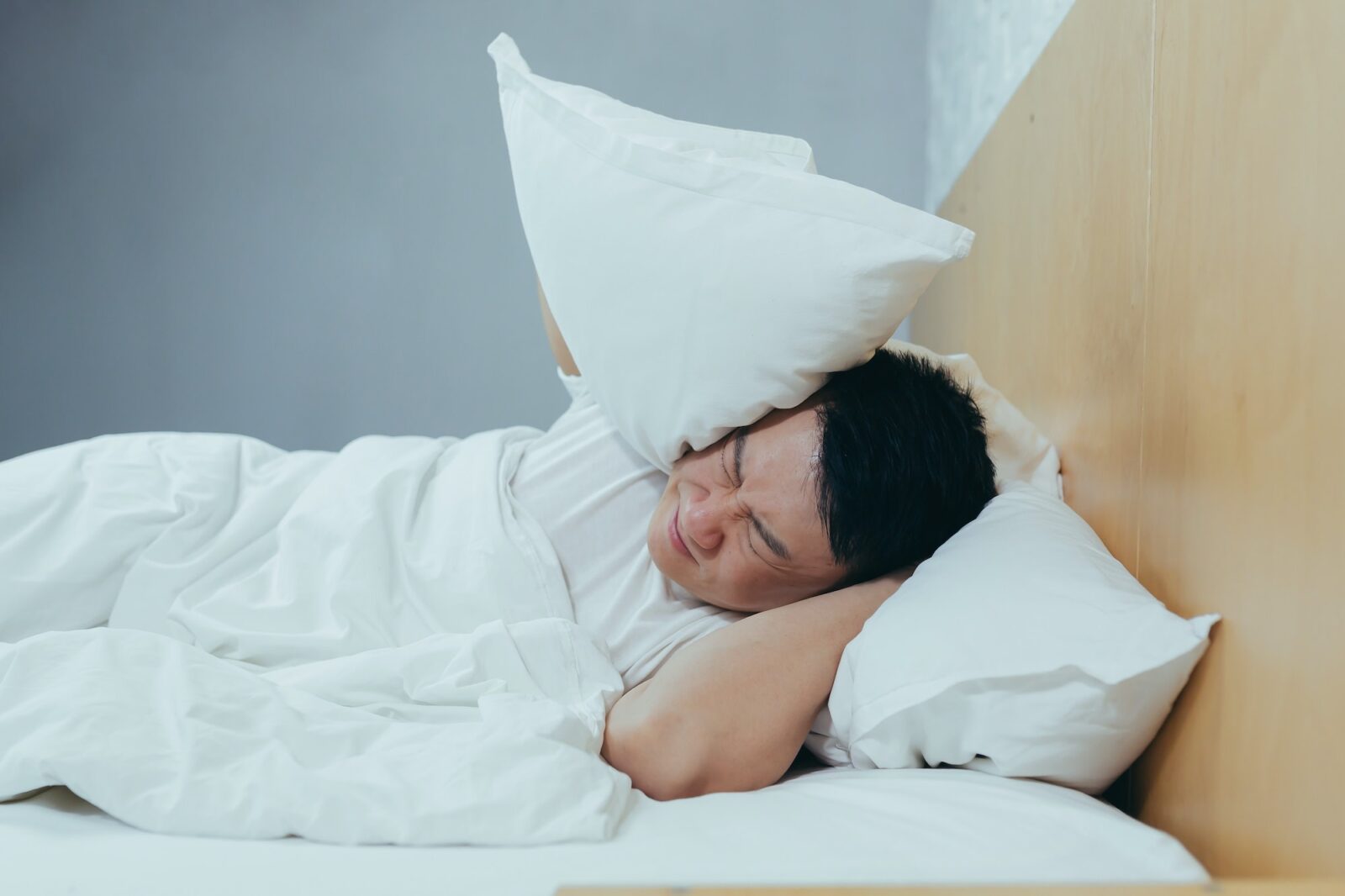 A man at home tries to fall asleep, noisy neighbors interfere with sleep