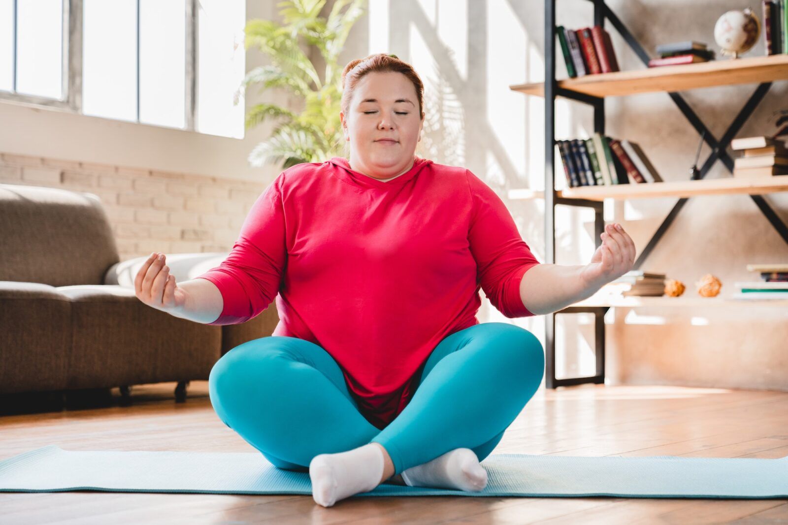 Plump obese caucasian fat woman meditating in sporty outfit at home. Fat woman sitting and relaxing