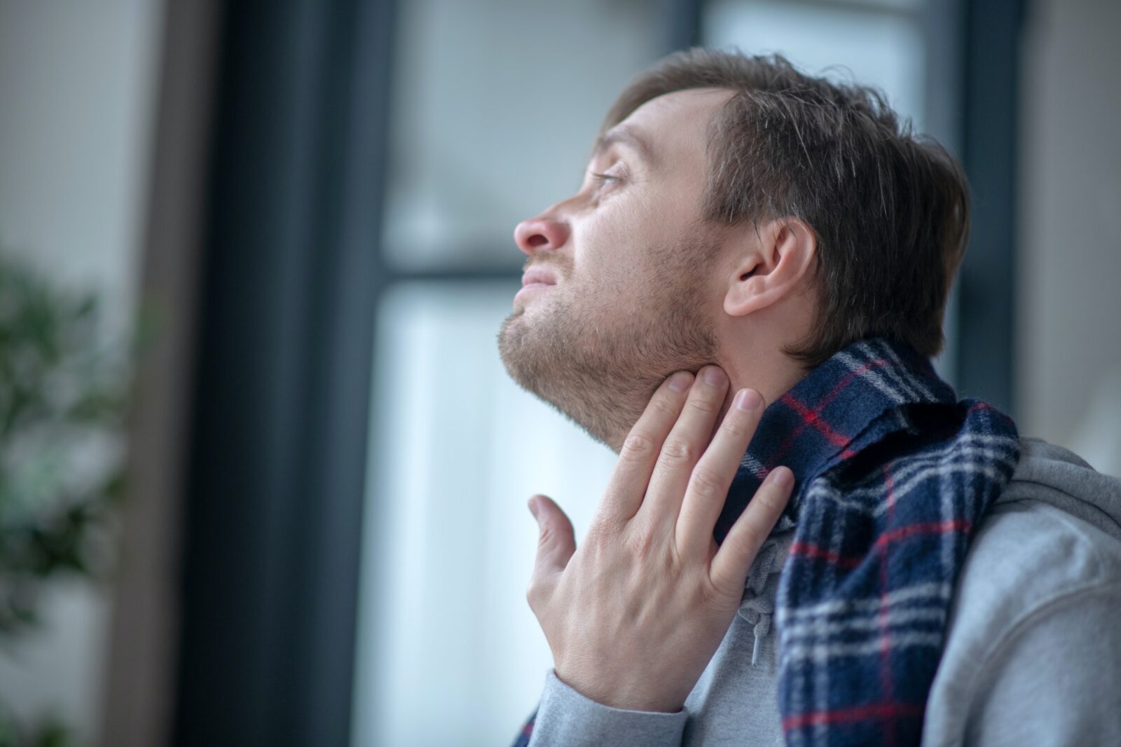 Dark-haired man wearing scarf while having tonsillitis