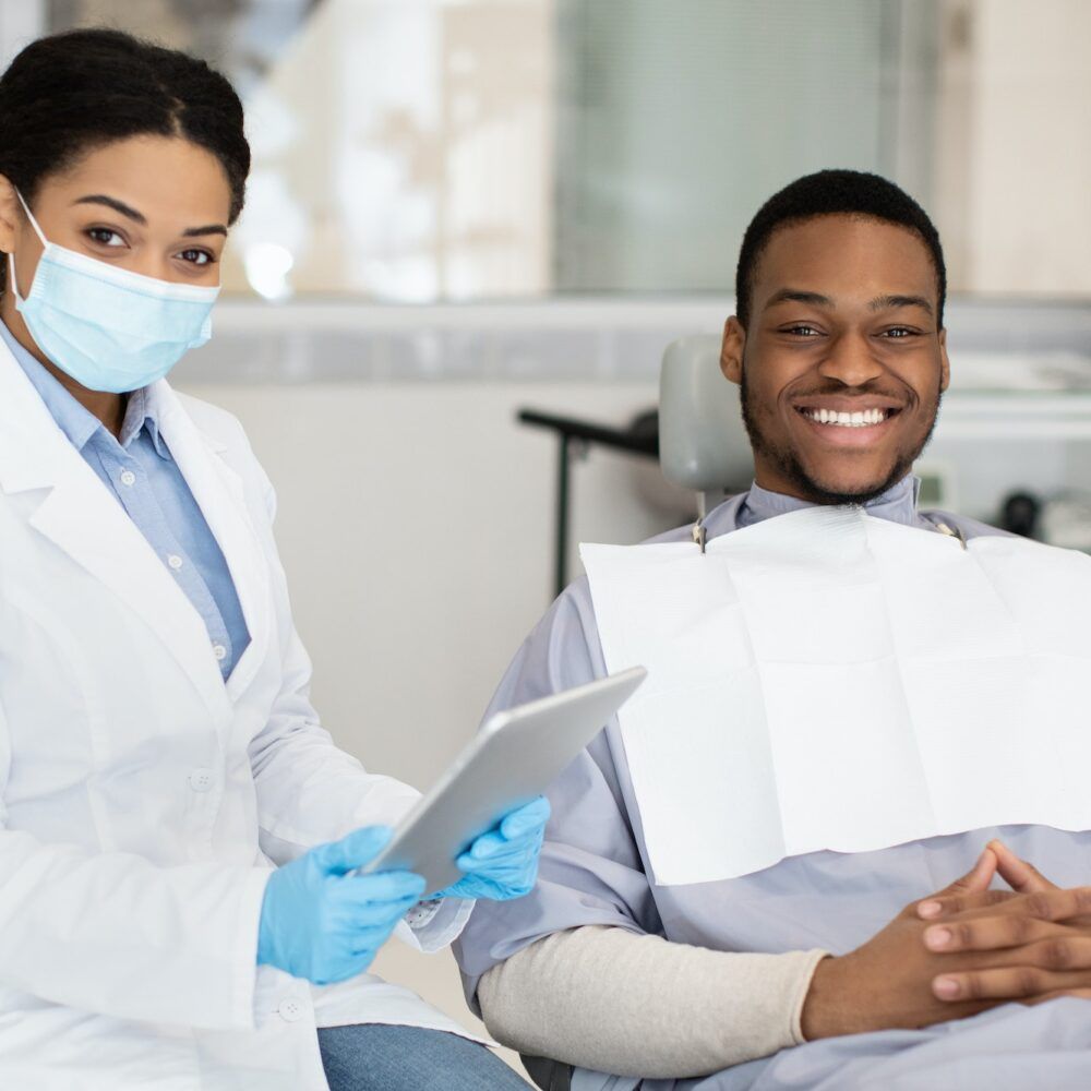 Dental Insurance Concept. Black Dentist Woman And Male Patient Posing In Clinic