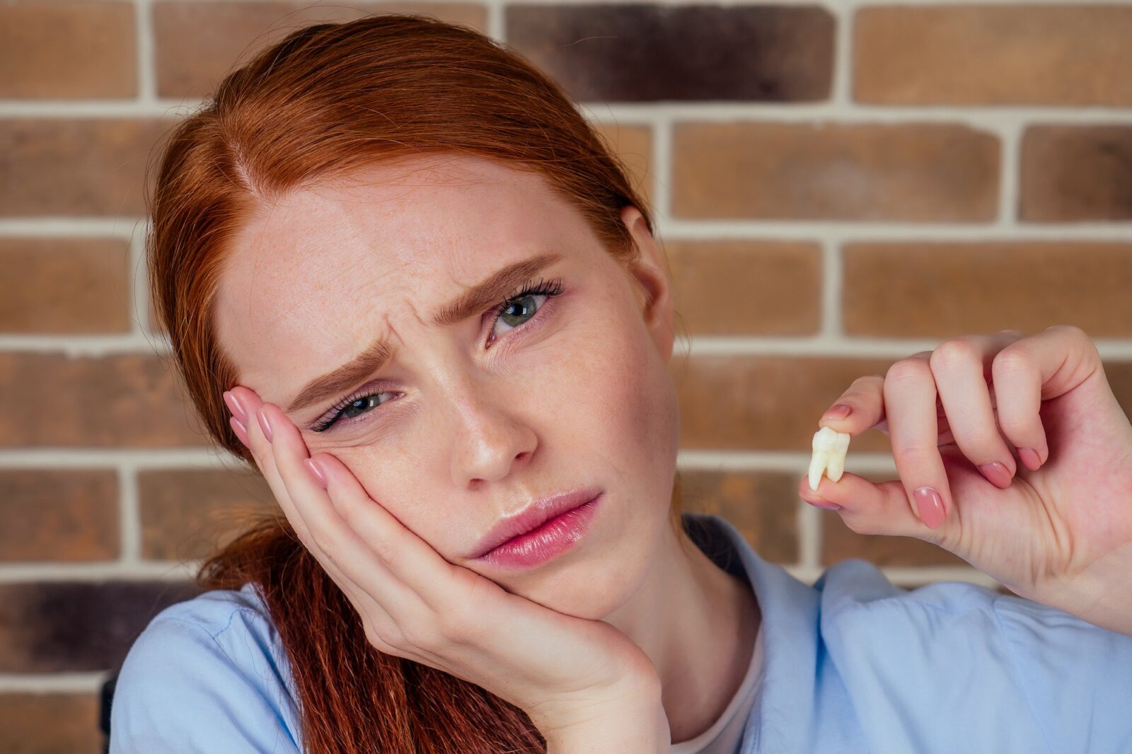 Redhaired ginger female with pain grimace holding white wisdom tooth