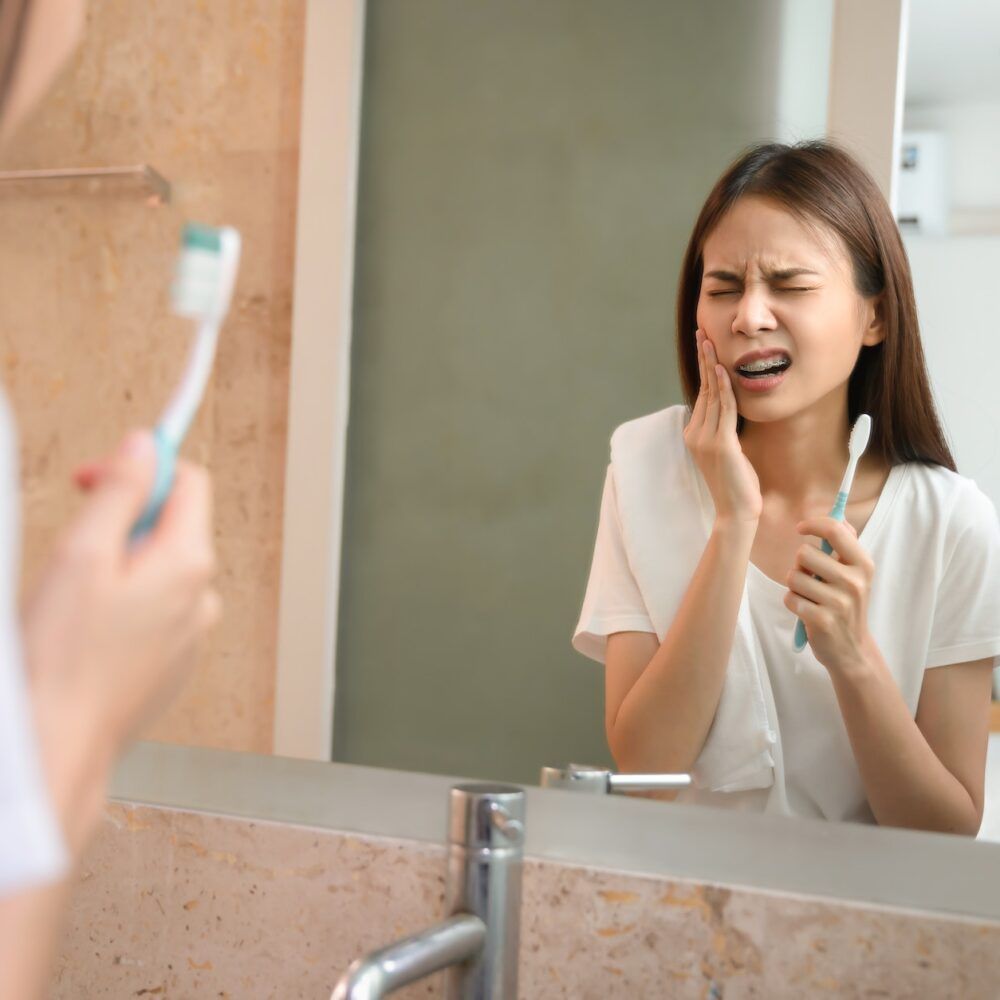 Young Asian woman brushing teeth with sensitive teeth and hands touch the cheeks.