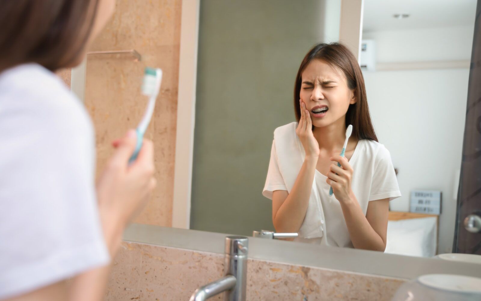 Young asian woman brushing teeth with sensitive teeth and hands touch the cheeks.