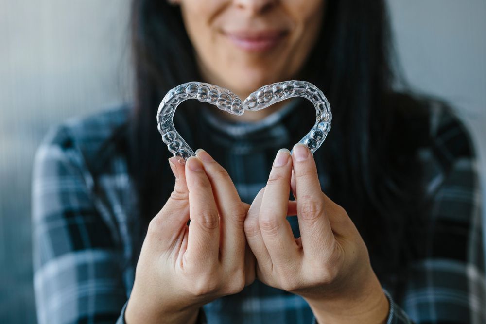 a woman holding a clear orthodontic aligners in the shape of a heart