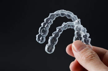 Hand holding two transparent retainers on black background. Invisalign orthodontics concept